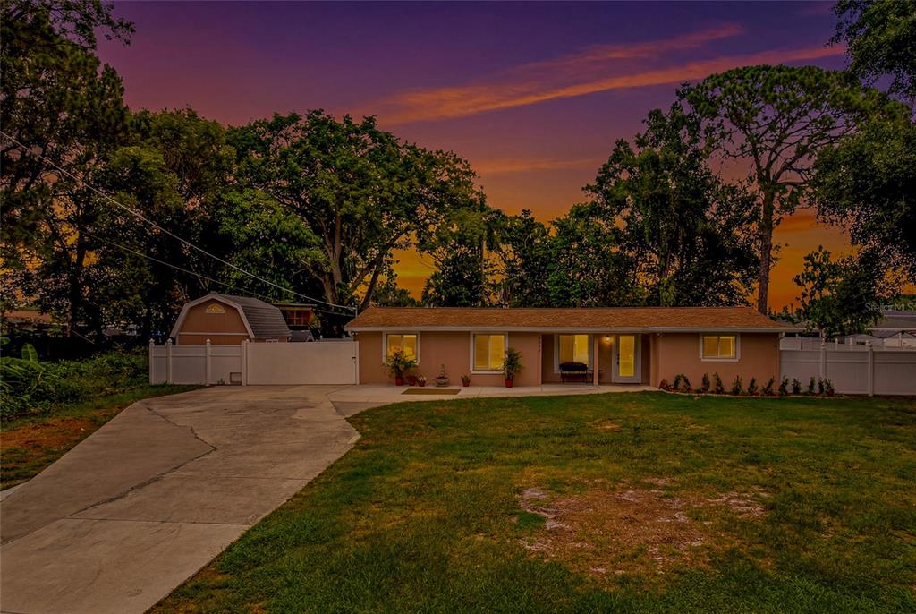 A single-story house with a concrete driveway and a detached shed under a sunset sky — 8205 WESTRIDGE DRIVE, TAMPA, FL