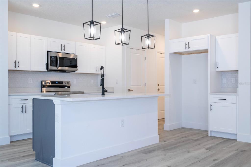 A modern kitchen features white cabinets, a gray island, stainless steel appliances, and pendant lighting — 2660 BREWSTER ROAD, NORTH PORT, FL
