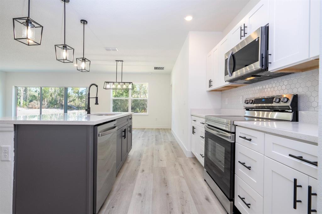 A modern kitchen features white cabinets, a dark gray island, and stainless steel appliances — 2660 BREWSTER ROAD, NORTH PORT, FL