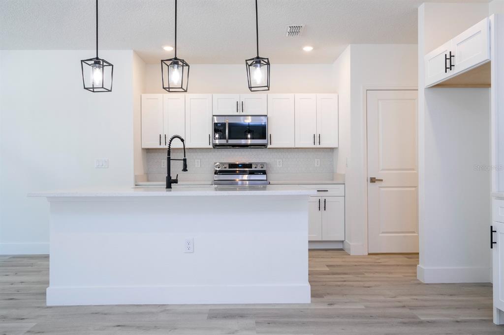A modern kitchen features white cabinets, stainless steel appliances, a center island, and pendant lighting — 2660 BREWSTER ROAD, NORTH PORT, FL