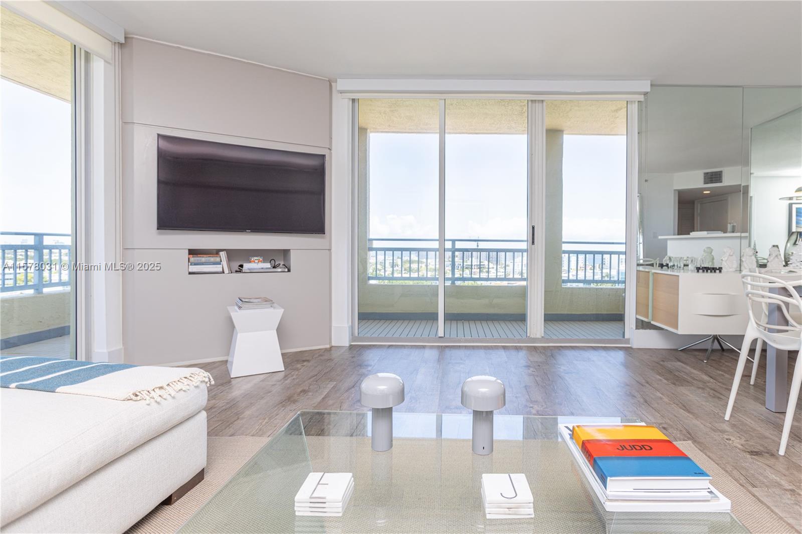 A living room features a wall-mounted television, glass sliding doors, and a glass coffee table — 90 Alton Rd # 1411, Miami Beach FL 33139, MIAMI BEACH, FL