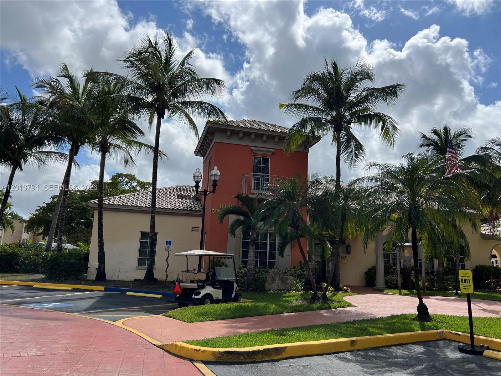 A golf cart is parked in front of a tan and orange building with palm trees — 8373 Lake Dr # 202, Doral FL 33166, DORAL, FL