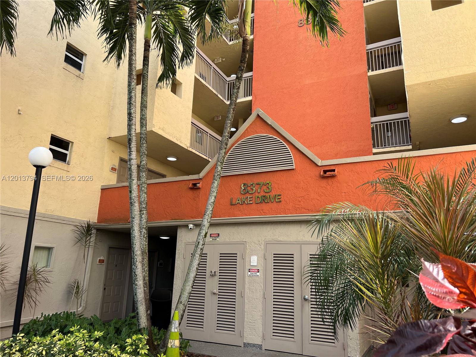 The exterior of a multi-story apartment building features orange and yellow stucco walls — 8373 Lake Dr # 202, Doral FL 33166, DORAL, FL