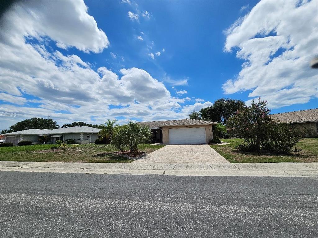 A single-story house with a white garage door and a paved driveway under a cloudy sky — 708 BRANNEN CIRCLE, SUN CITY CENTER, FL