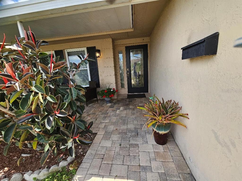A paved walkway leads to a front entrance with a glass door and potted plants — 708 BRANNEN CIRCLE, SUN CITY CENTER, FL