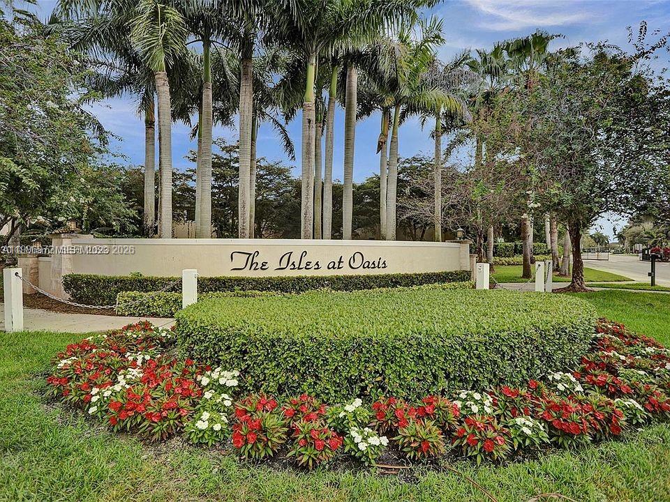 A stone entrance sign for The Isles at Oasis sits behind a manicured hedge and flowers — 164 NE 23rd Ter, Homestead FL 33033, HOMESTEAD, FL