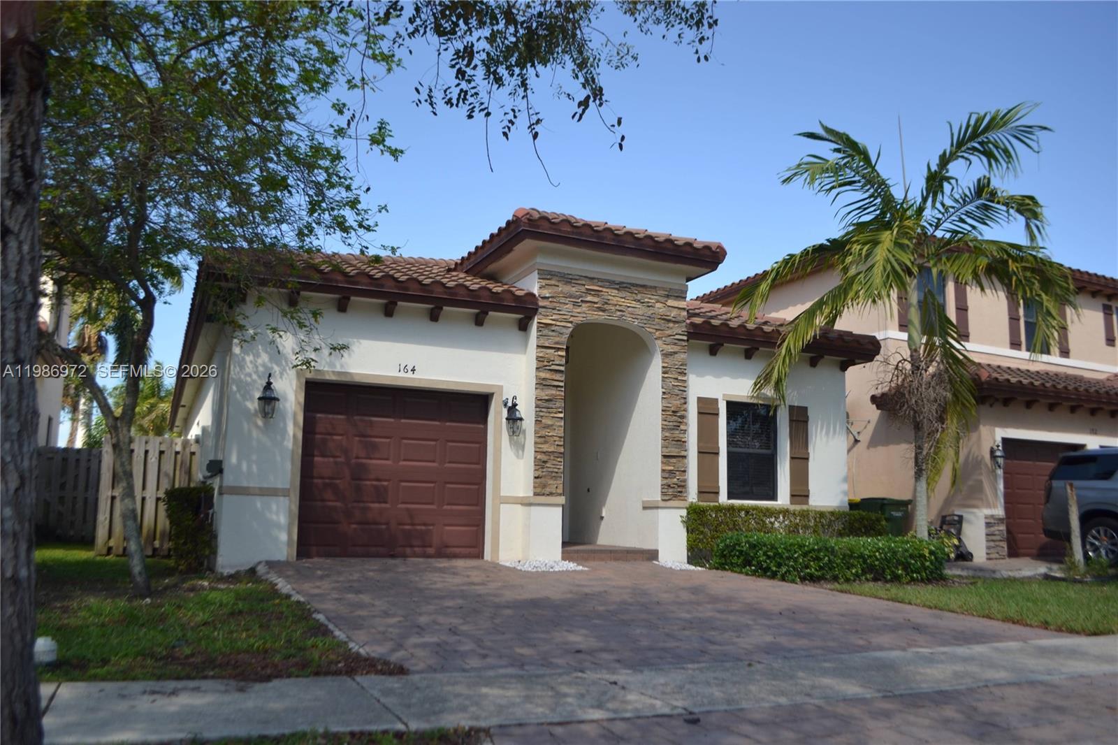 A single-story house with a brown garage door, stone entryway, and a tiled roof — 164 NE 23rd Ter, Homestead FL 33033, HOMESTEAD, FL
