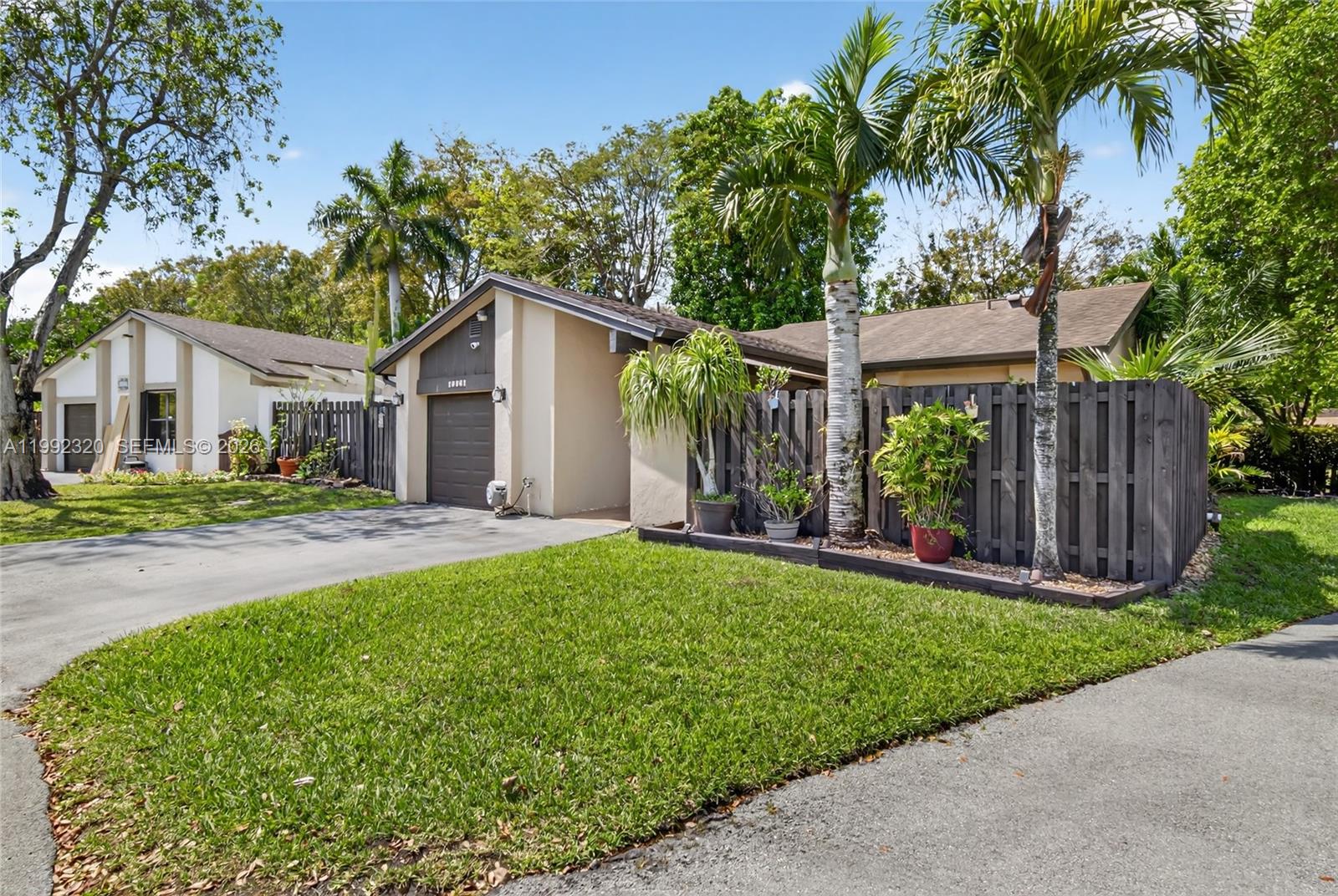 A single-story house with a brown garage, a wooden fence, and palm trees in front — 10861 SW 132nd Cir Ct, Miami FL 33186, MIAMI, FL