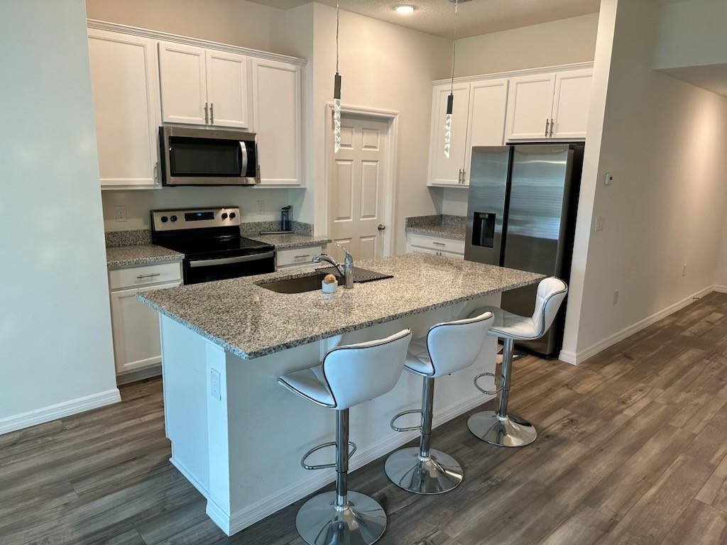 A kitchen features white cabinets, granite countertops, a center island with bar stools, and appliances — 1099 NE Dania Circle, Palm Bay FL 32905, PALM BAY, FL