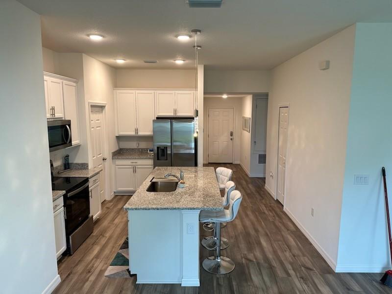 A kitchen with white cabinets, granite countertops, a center island, and wood-look flooring — 1099 NE Dania Circle, Palm Bay FL 32905, PALM BAY, FL