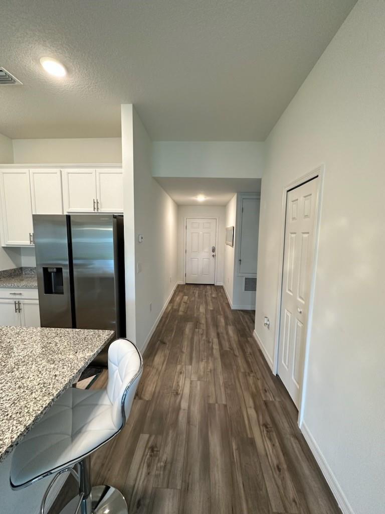 A hallway with wood-look flooring leads from a kitchen with granite countertops to an entryway — 1099 NE Dania Circle, Palm Bay FL 32905, PALM BAY, FL
