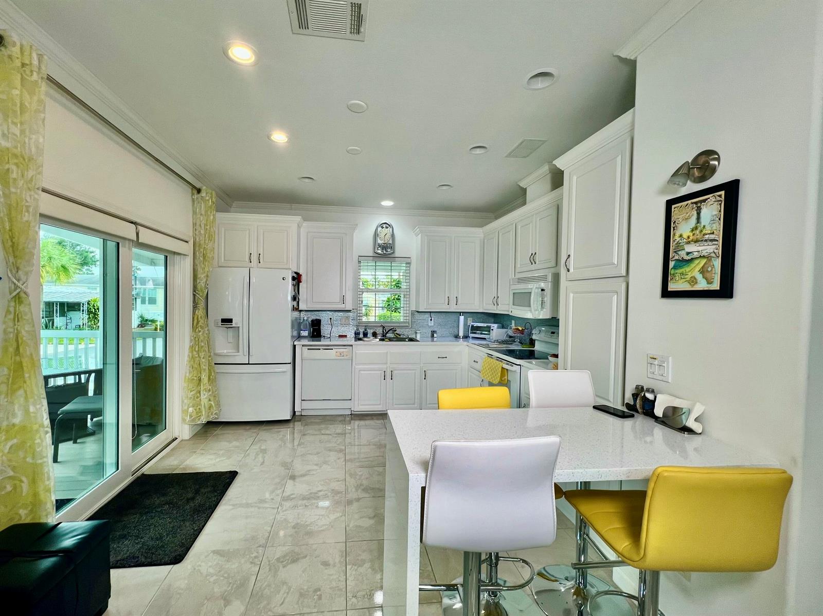 A bright kitchen features white cabinetry, a quartz-topped island, and a sliding glass door — 413 Hibiscus Drive, Deerfield Beach FL 33442, DEERFIELD BEACH, FL