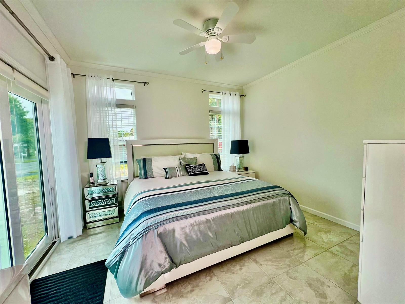 A bedroom features a king bed with blue bedding, mirrored nightstands, and a ceiling fan — 413 Hibiscus Drive, Deerfield Beach FL 33442, DEERFIELD BEACH, FL