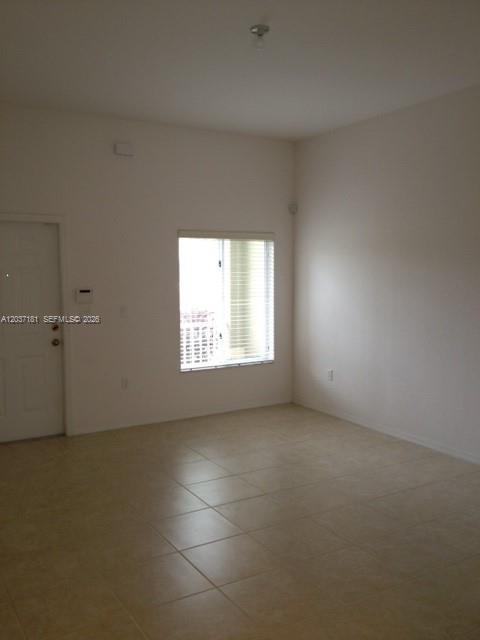 An empty room with beige tile flooring, a window with blinds, and a white door — 1657 SE 23rd Way # 1657, Homestead FL 33035, HOMESTEAD, FL