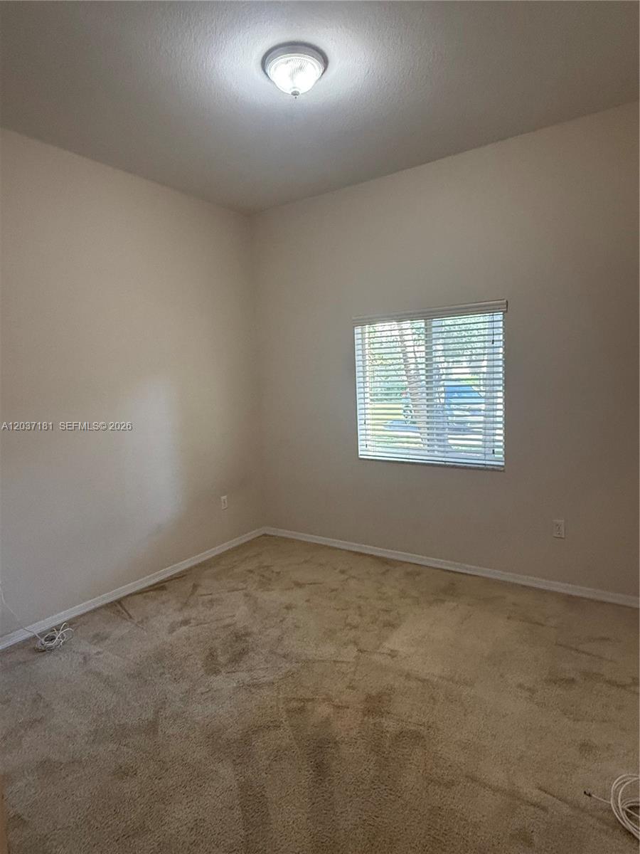 An empty bedroom features beige carpet, light-colored walls, a ceiling light, and a window — 1657 SE 23rd Way # 1657, Homestead FL 33035, HOMESTEAD, FL