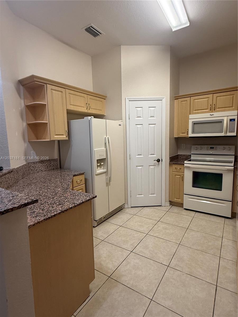 A kitchen features light wood cabinets, granite countertops, white appliances, and beige tile flooring — 1657 SE 23rd Way # 1657, Homestead FL 33035, HOMESTEAD, FL