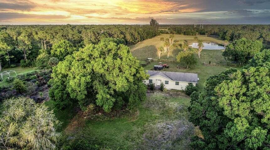 An aerial view shows a single-story house surrounded by large trees and a grassy field — 11470 Carlton Road, Port St. Lucie FL 34987, PORT ST. LUCIE, FL