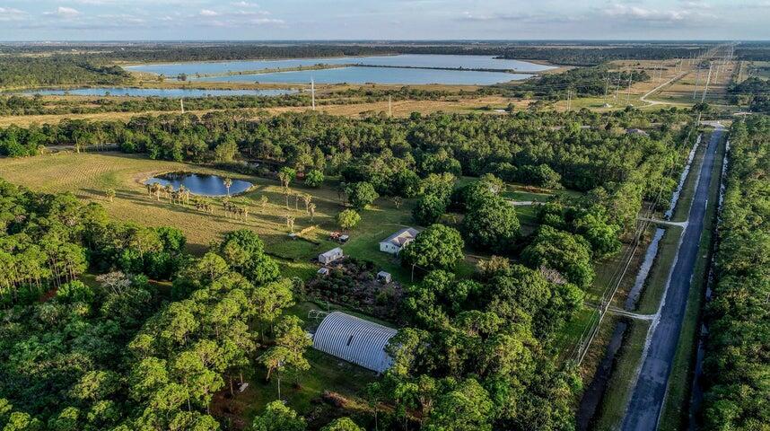 An aerial view shows a rural property with a metal Quonset hut, house, and pond — 11470 Carlton Road, Port St. Lucie FL 34987, PORT ST. LUCIE, FL