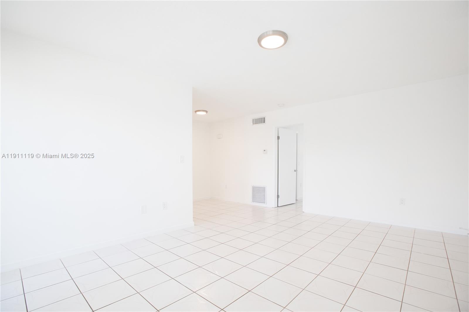 A bright, empty room features white walls, white tiled flooring, and two flush-mount ceiling lights — 1060 NE 78th St Rd # 10, Miami FL 33138, MIAMI, FL