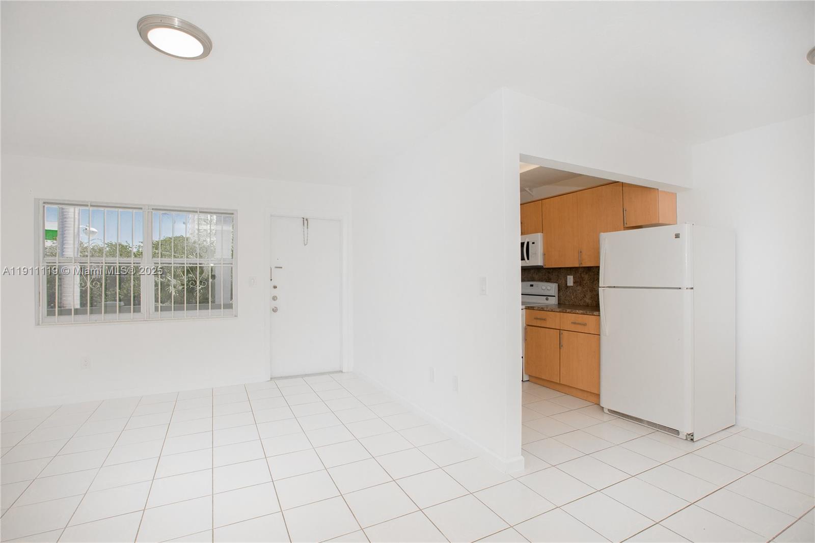 A white-tiled living area features a white front door and an adjacent galley kitchen — 1060 NE 78th St Rd # 10, Miami FL 33138, MIAMI, FL