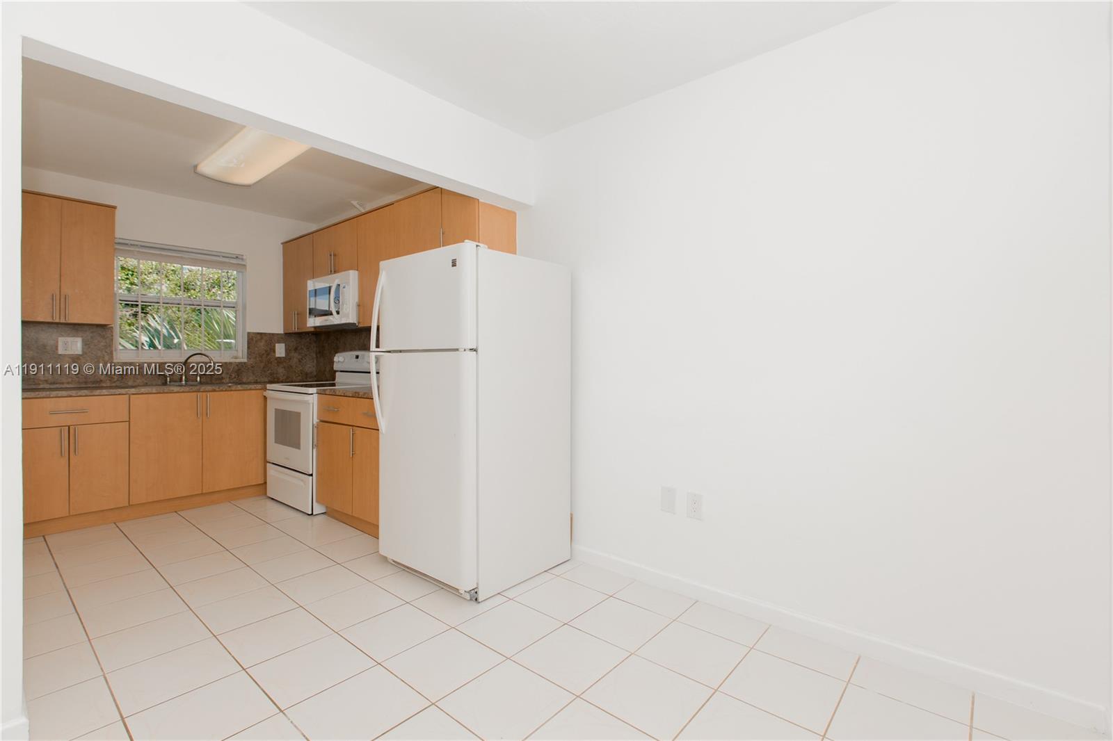 A kitchen features light wood cabinets, white appliances, and white tile flooring — 1060 NE 78th St Rd # 10, Miami FL 33138, MIAMI, FL