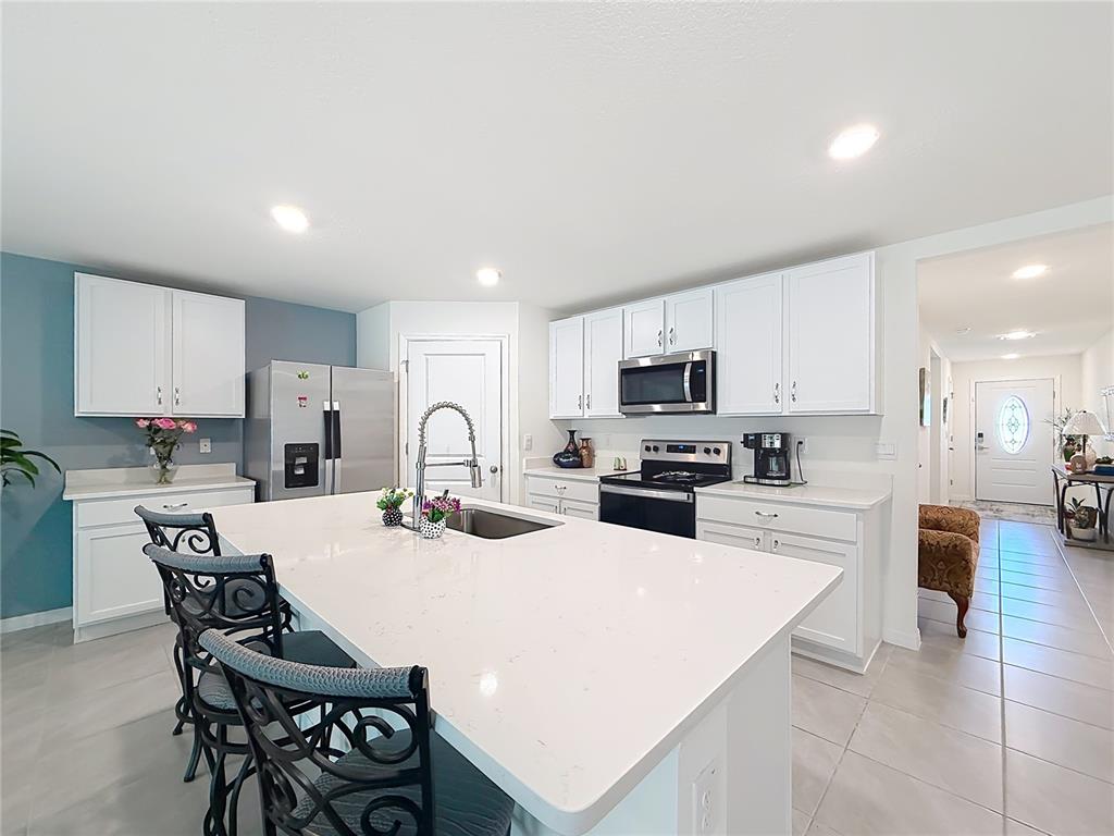 A kitchen features white cabinets, a large quartz island, and stainless steel appliances — 13677 SW 69TH TERRACE, OCALA, FL