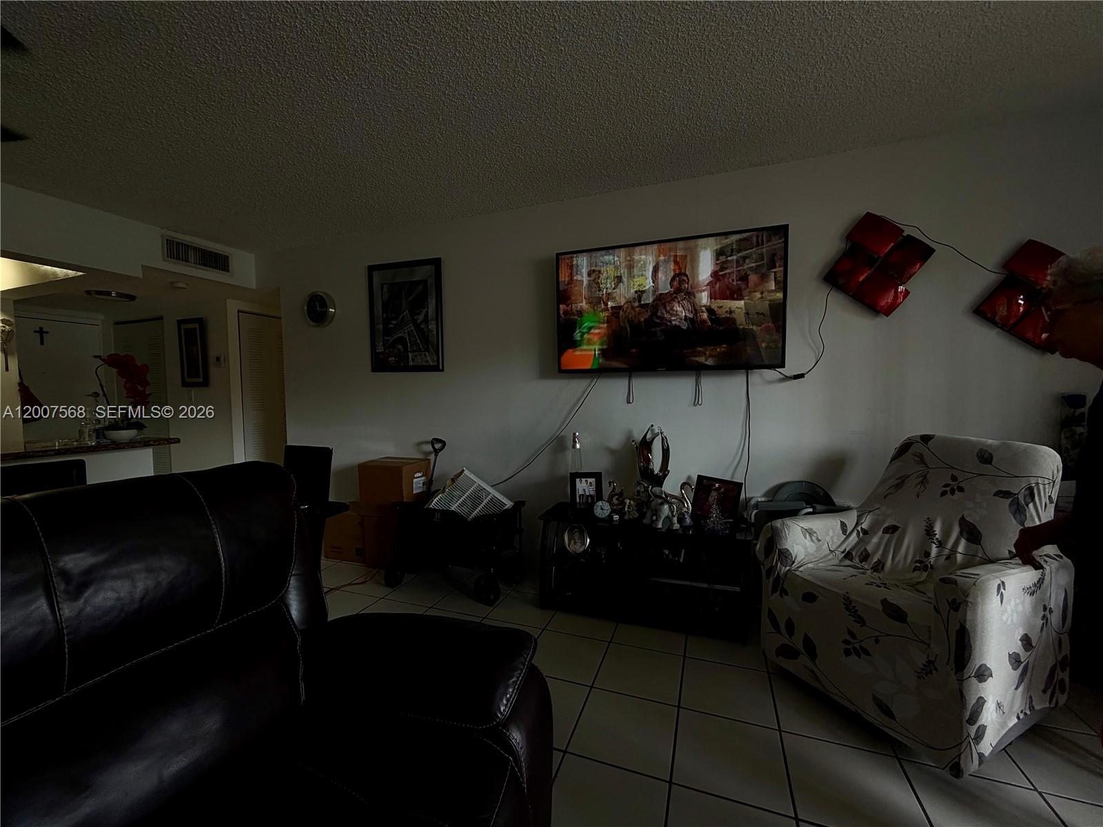 A living room features a wall-mounted television, tiled flooring, and a patterned armchair — 5201 NW 7th St # 104, Miami FL 33126, MIAMI, FL