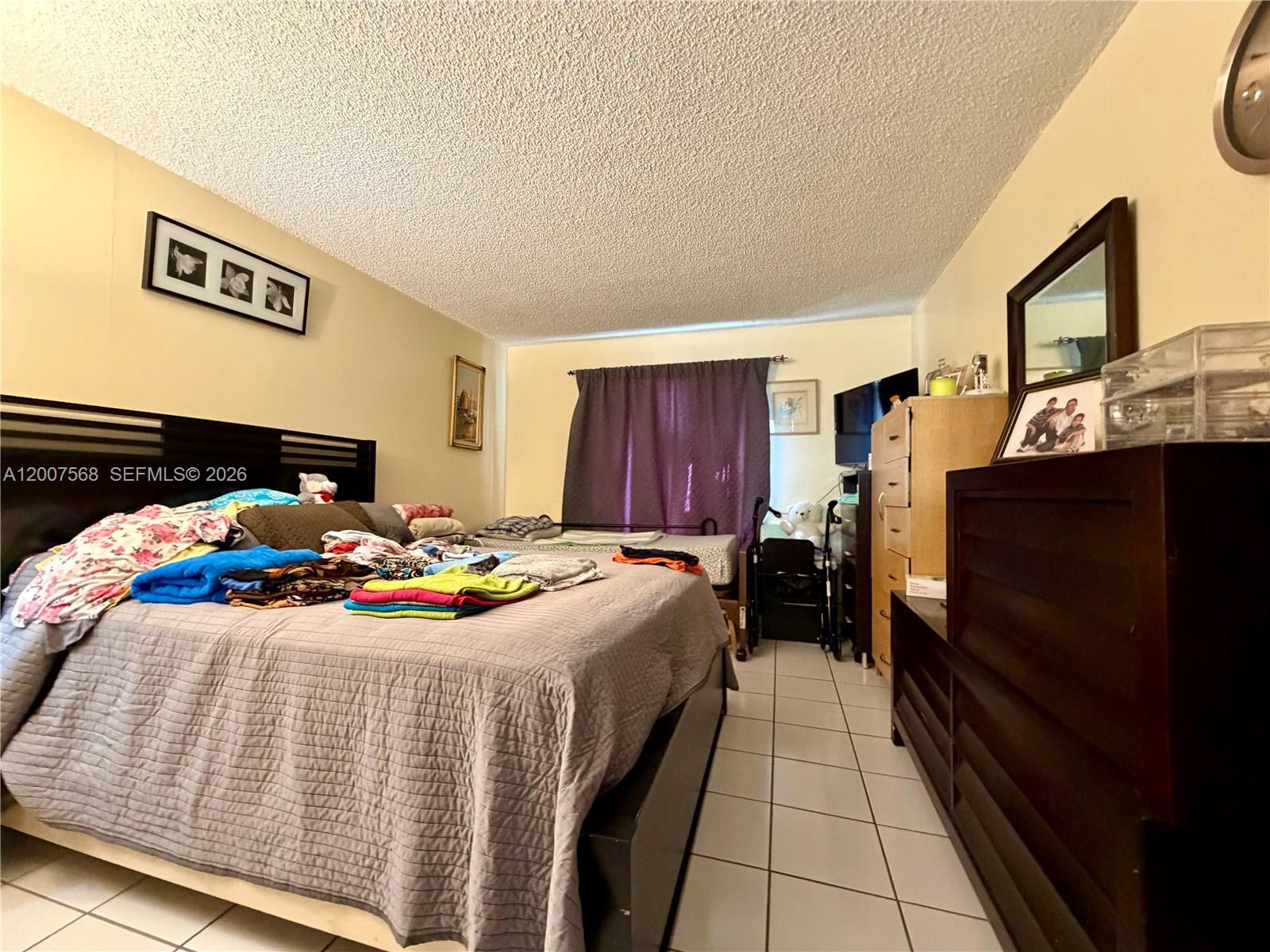 A bedroom features a large bed, tile flooring, a dresser, and a window with curtains — 5201 NW 7th St # 104, Miami FL 33126, MIAMI, FL