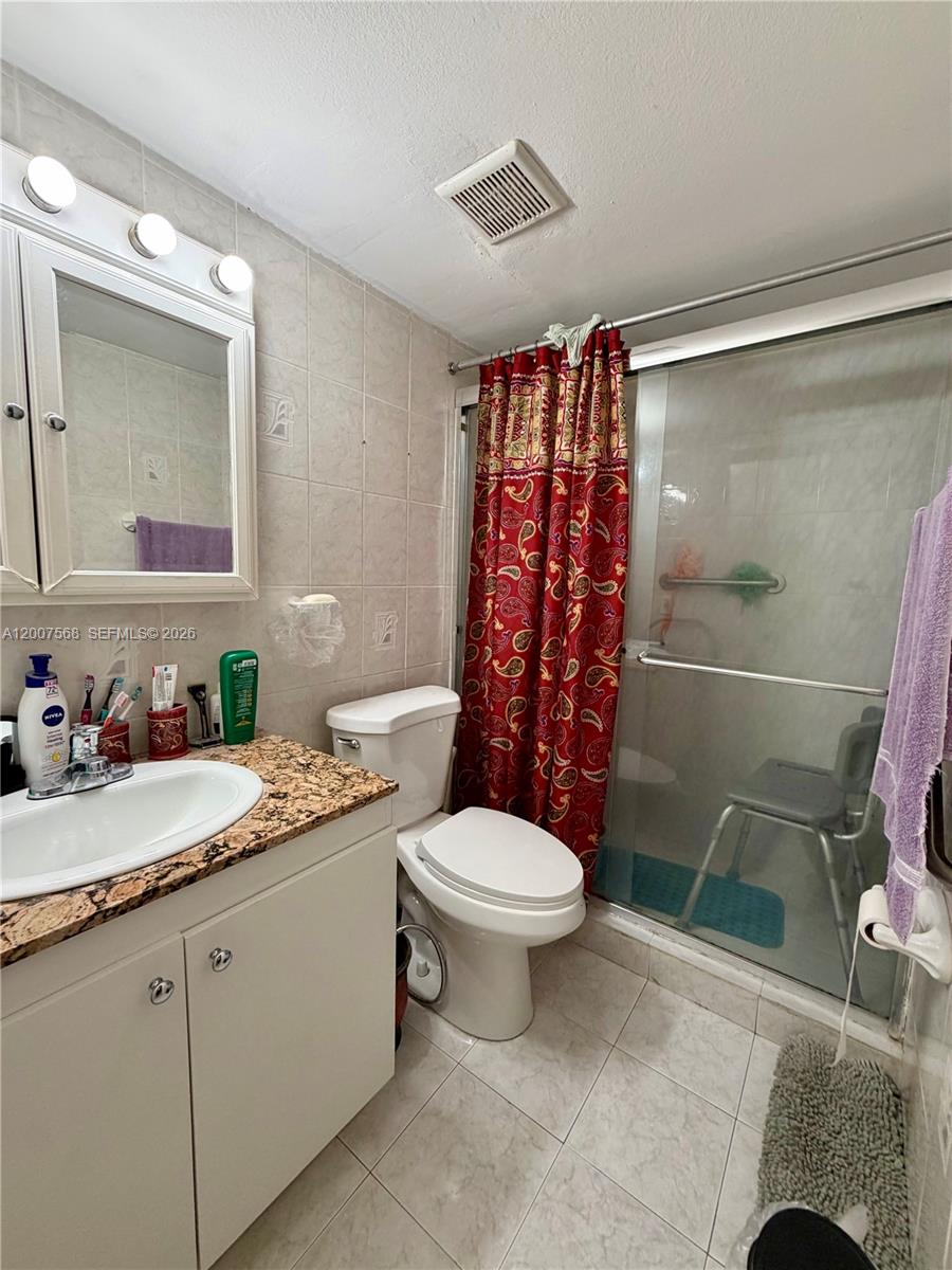 A bathroom features a vanity with a granite countertop, a toilet, and a glass-enclosed shower — 5201 NW 7th St # 104, Miami FL 33126, MIAMI, FL