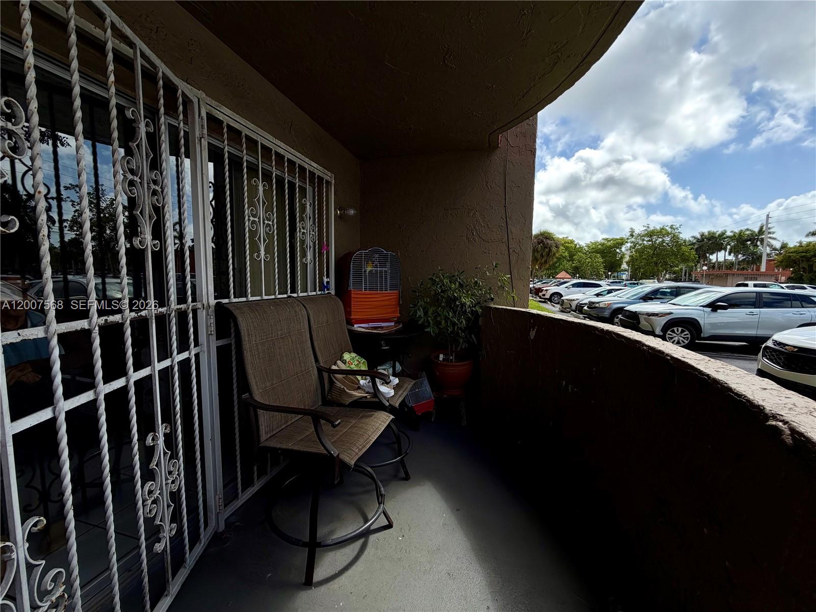 A covered balcony features two chairs, a birdcage, a potted plant, and security bars — 5201 NW 7th St # 104, Miami FL 33126, MIAMI, FL