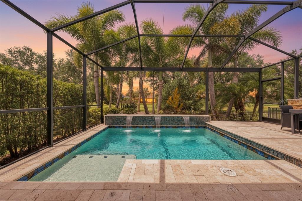 A screened-in patio features a swimming pool with three water fountains and stone decking — 8467 NANDINA DRIVE, SARASOTA, FL