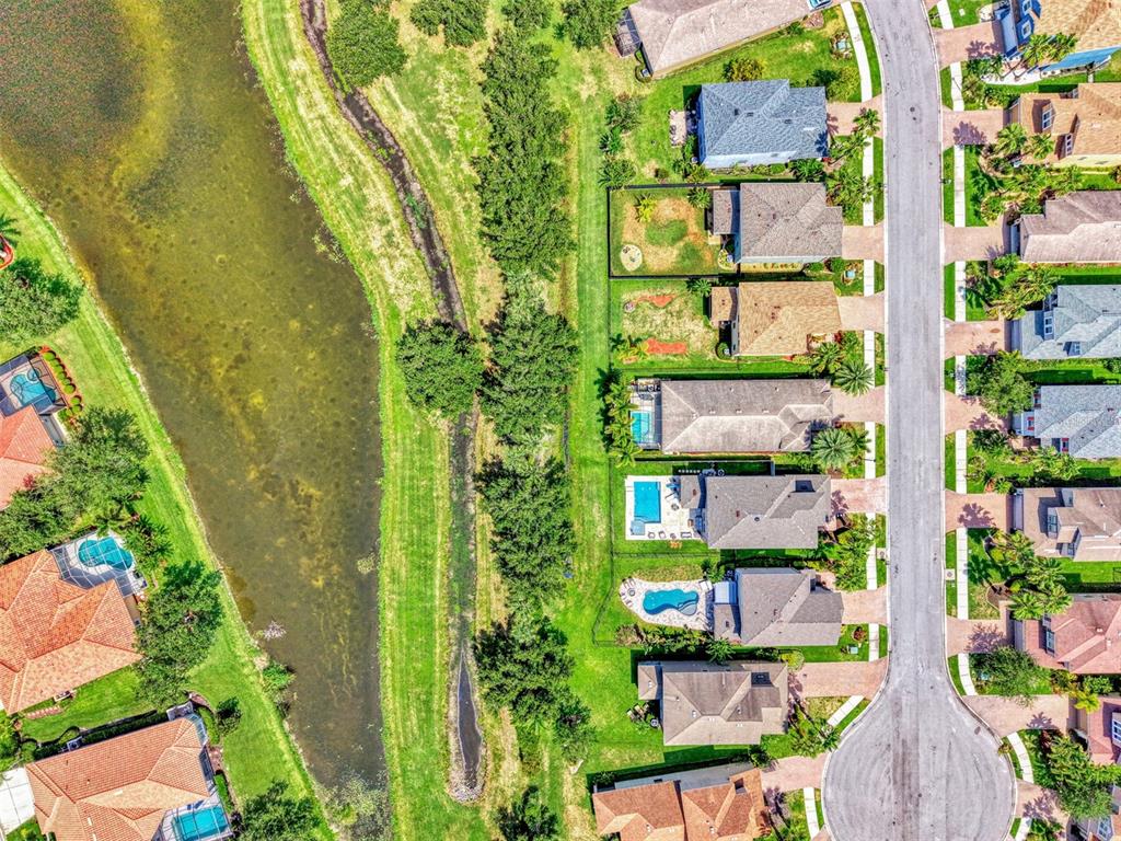 An aerial view shows suburban houses with swimming pools bordering a narrow canal and pond — 8467 NANDINA DRIVE, SARASOTA, FL