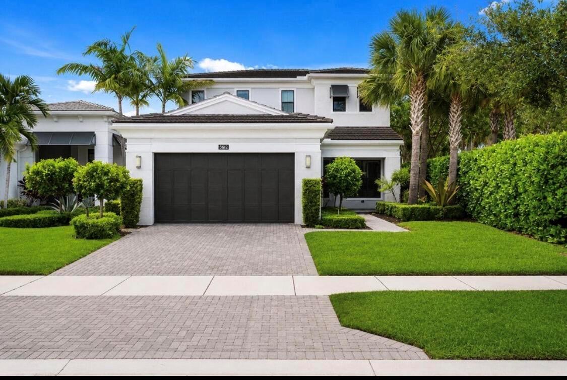 A two-story white house features a dark garage door, a paved driveway, and manicured landscaping — 5603 Delacroix Terrace, Palm Beach Gardens FL 33418, PALM BEACH GARDENS, FL