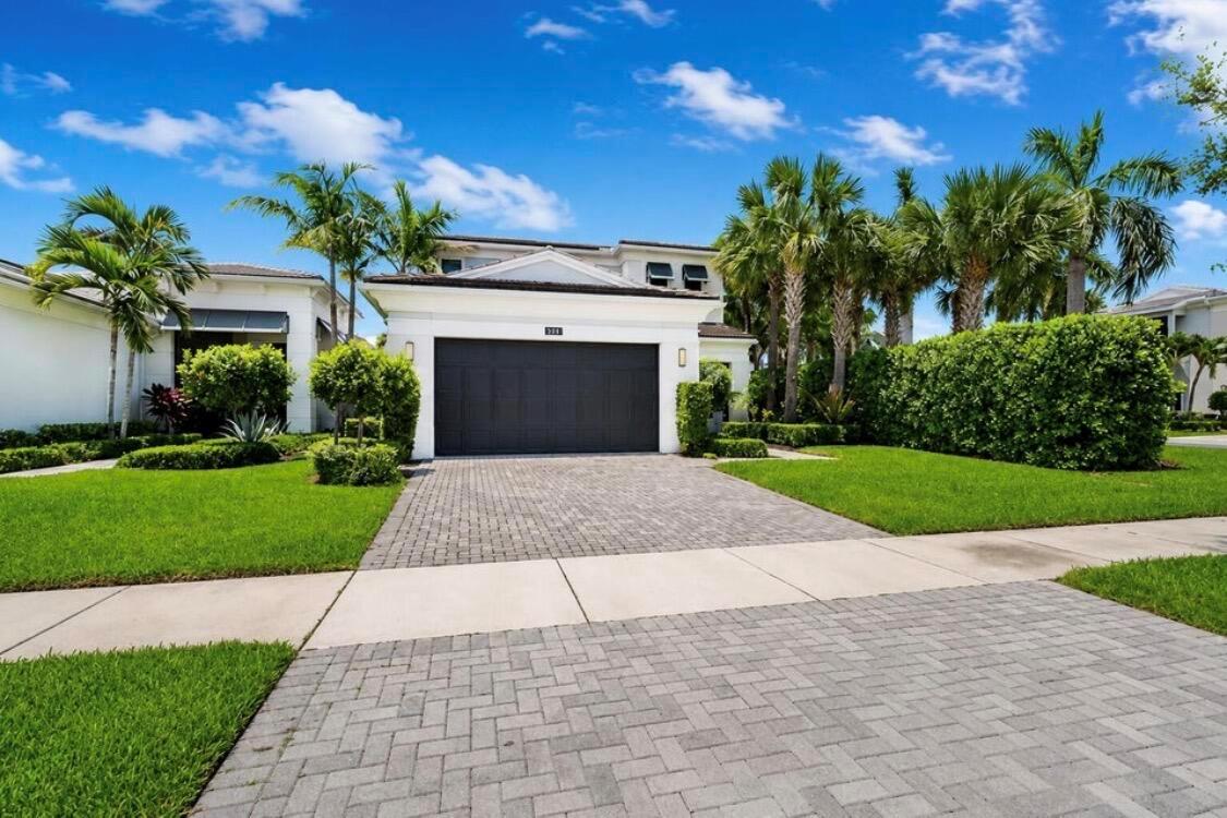 A white house with a dark garage door and a paved driveway under a blue sky — 5603 Delacroix Terrace, Palm Beach Gardens FL 33418, PALM BEACH GARDENS, FL