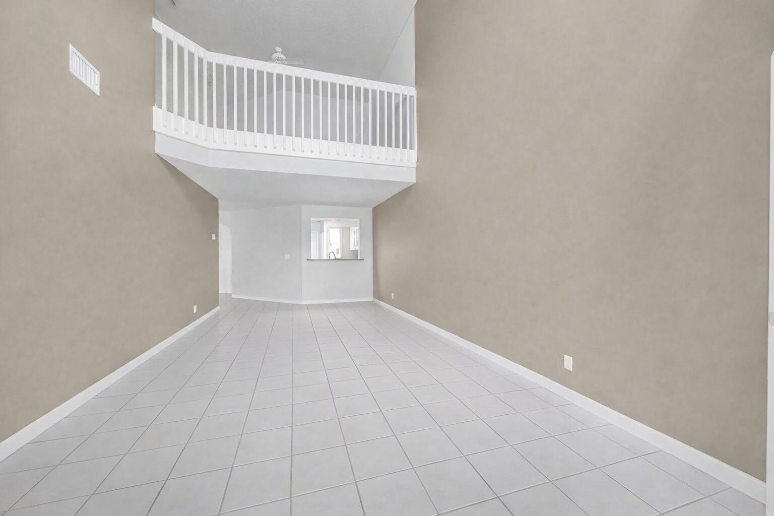 An empty room with light-colored tile flooring, beige walls, and a white loft railing above — 9082 Boca Gardens Parkway # C, Boca Raton FL 33496, BOCA RATON, FL