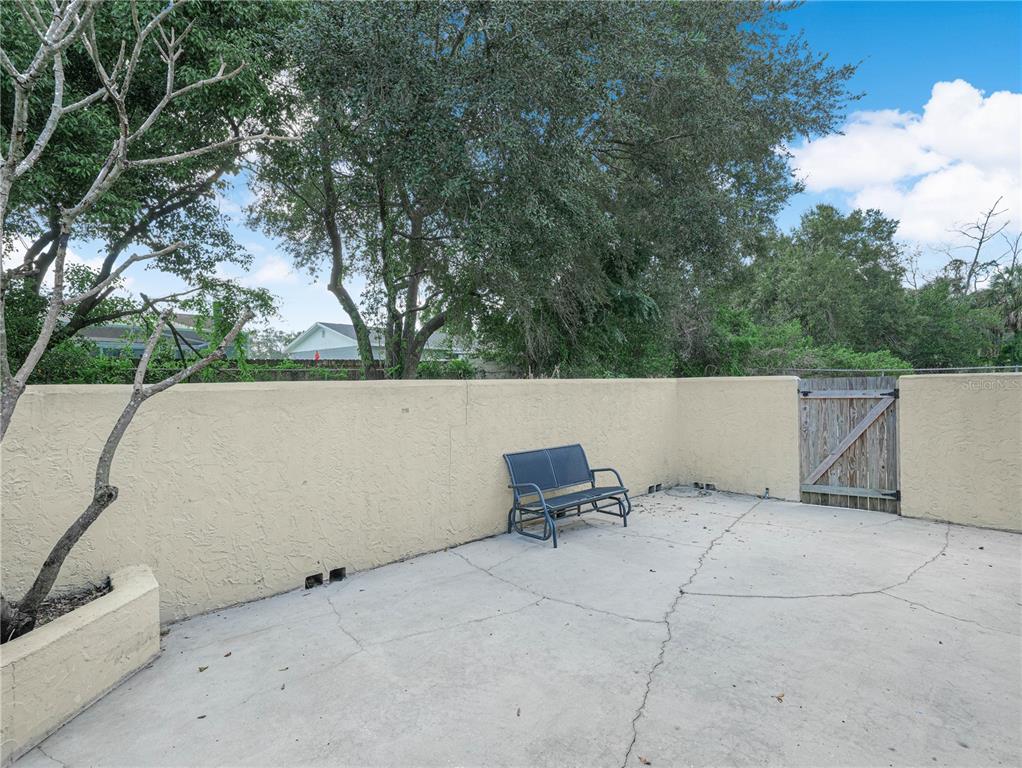 A concrete patio features a metal bench against a stucco wall and a wooden gate — 1880 N CRYSTAL LAKE DRIVE UNIT 18, LAKELAND, FL