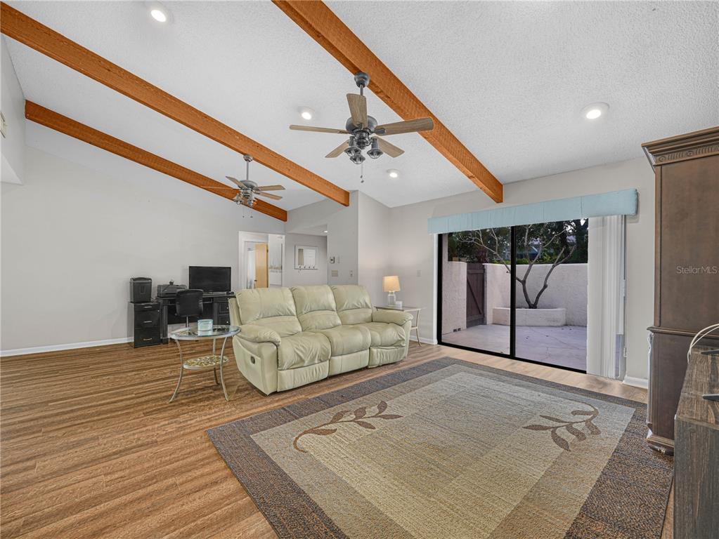 A living room features wood-look flooring, vaulted ceilings with exposed beams, ceiling fans, and sliding glass doors — 1880 N CRYSTAL LAKE DRIVE UNIT 18, LAKELAND, FL