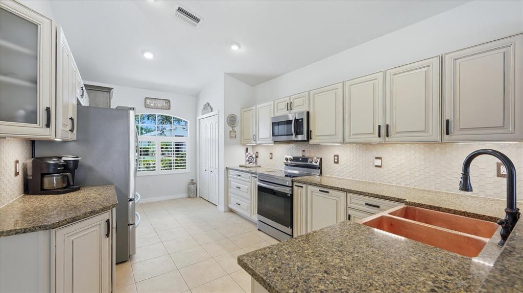 A kitchen features light-colored cabinetry, granite countertops, a copper sink, and stainless steel appliances — 8222 HAVEN HARBOUR WAY, BRADENTON, FL