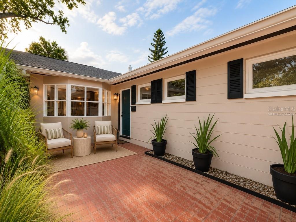A brick patio features two chairs, a small table, and potted plants against a house exterior — 8161 22ND AVENUE N, ST PETERSBURG, FL