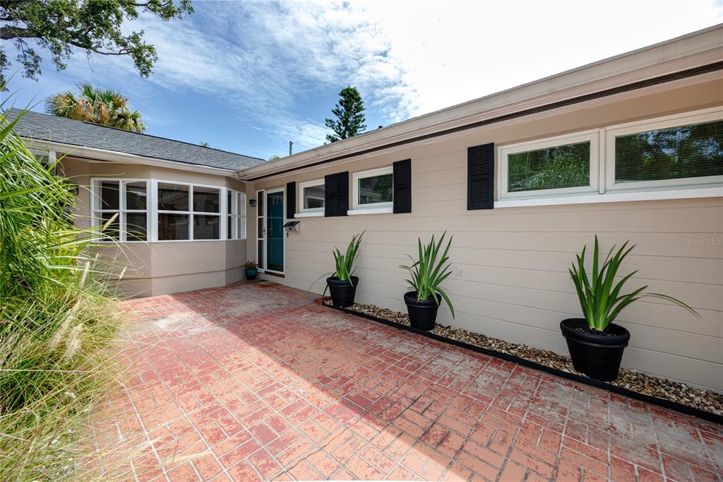 A brick patio leads to the entrance of a house with beige siding and shutters — 8161 22ND AVENUE N, ST PETERSBURG, FL