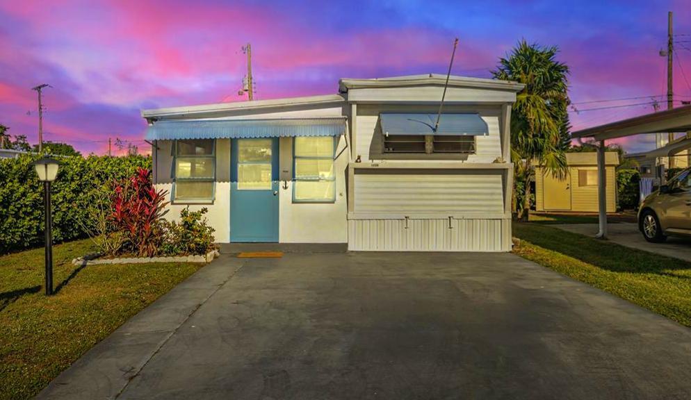 A single-story mobile home with a blue door, metal awning, and a paved driveway — 14556 Glenview Drive, Delray Beach FL 33445, DELRAY BEACH, FL