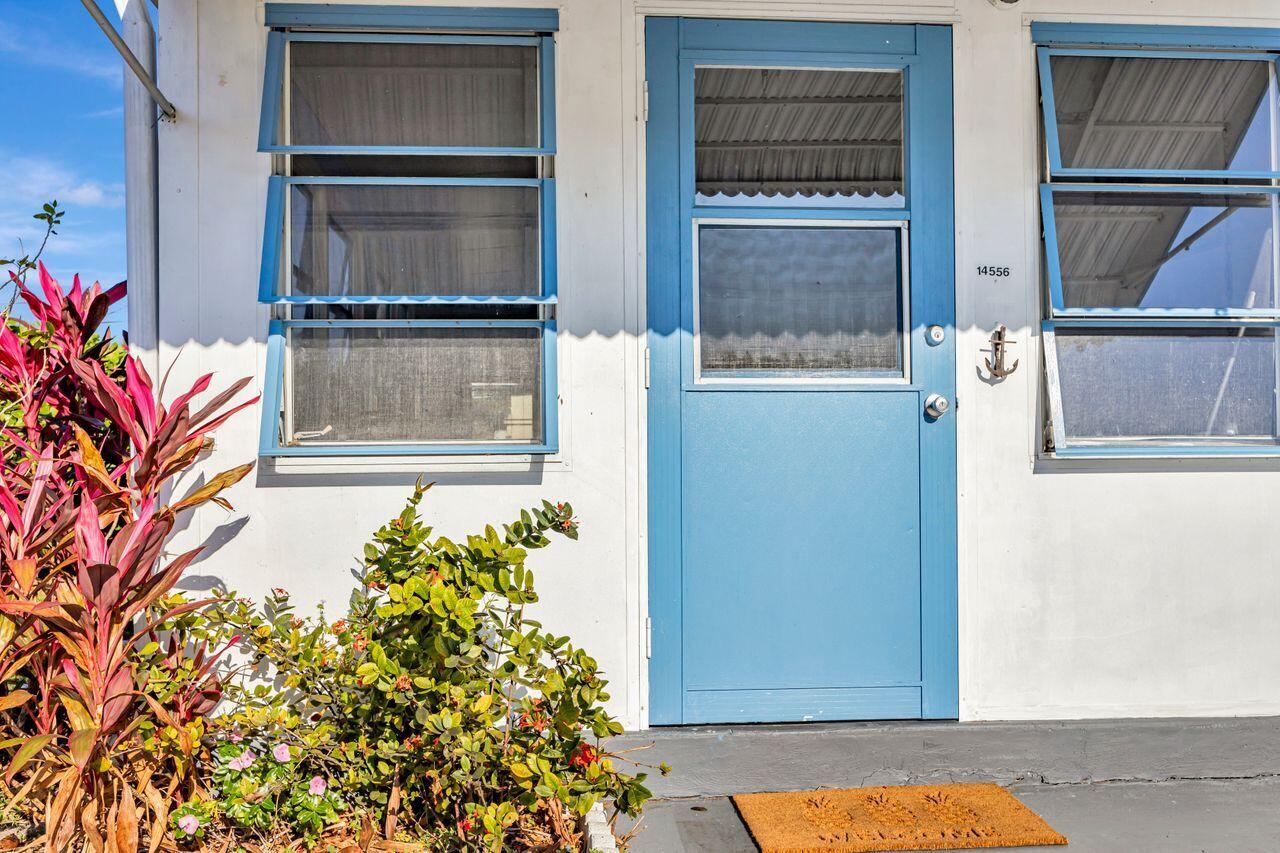 A white exterior wall features a blue door and two blue-framed louvered windows — 14556 Glenview Drive, Delray Beach FL 33445, DELRAY BEACH, FL