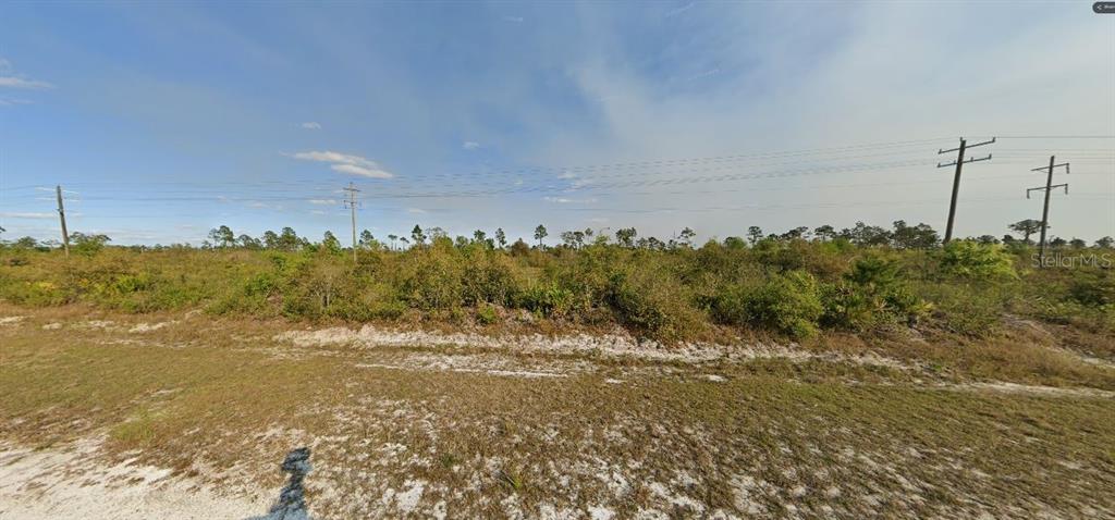 A vacant, grassy lot with scattered shrubs and several utility poles under a blue sky — ST PETERSBURG DRIVE, INDIAN LAKE ESTATES, FL