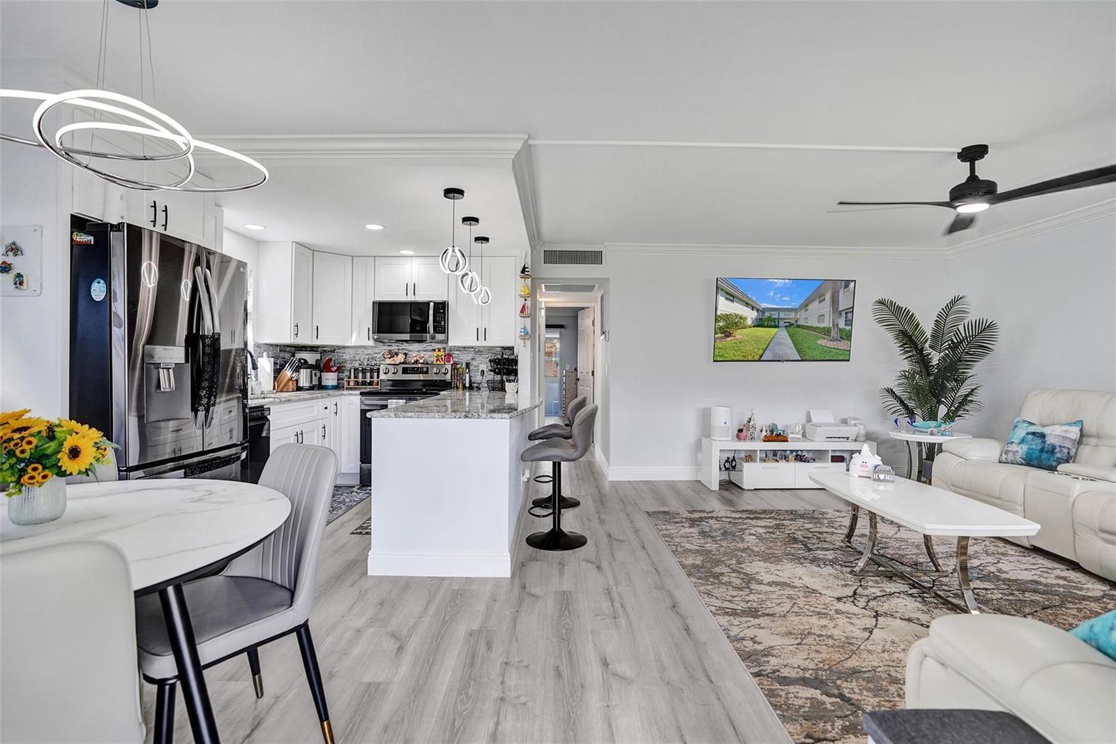 A modern open-concept kitchen and living area with white cabinetry, gray flooring, and a television — 356 Brittany H # 356, Delray Beach FL 33446, DELRAY BEACH, FL