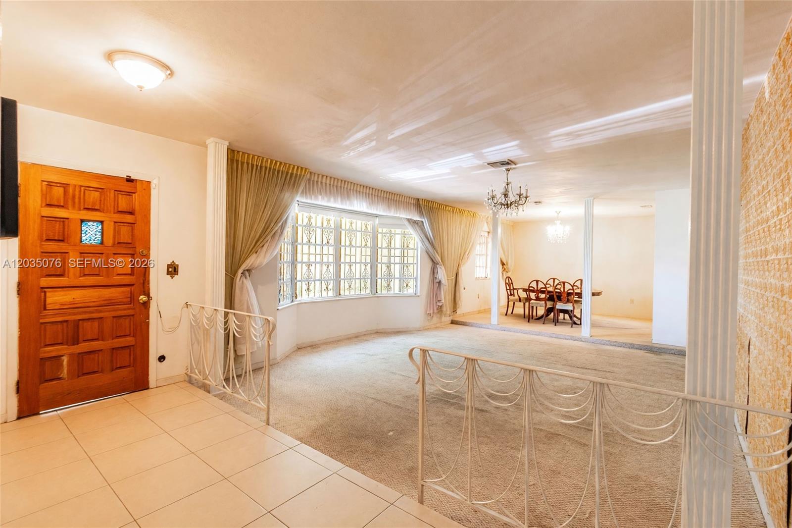 A sunken living room with carpeted floors, white metal railings, and a dining area beyond — 785 NE 155th St, Miami FL 33162, MIAMI, FL