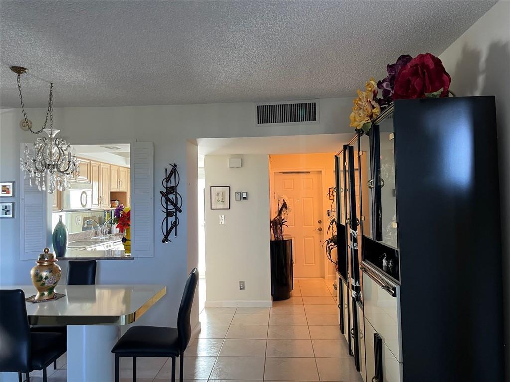 A dining area with a chandelier and pass-through window leads to an entryway with tile floors — 333 NE 21 Avenue # 304, Deerfield Beach FL 33441, DEERFIELD BEACH, FL