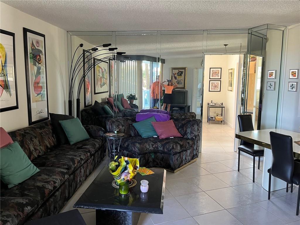 A living room features a mirrored wall, patterned sofa, black coffee table, and tile flooring — 333 NE 21 Avenue # 304, Deerfield Beach FL 33441, DEERFIELD BEACH, FL