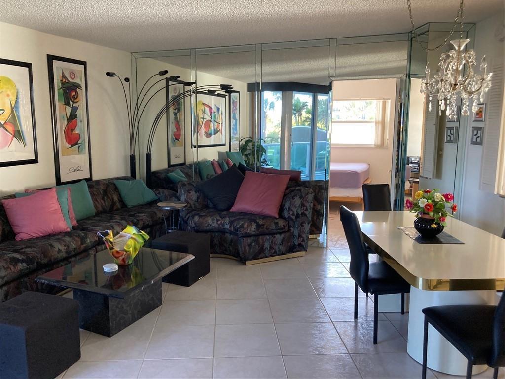 A living and dining area features mirrored walls, a patterned sectional sofa, and tile flooring — 333 NE 21 Avenue # 304, Deerfield Beach FL 33441, DEERFIELD BEACH, FL