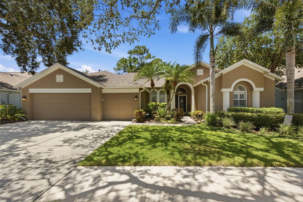 A single-story house with a tan exterior, a three-car garage, and a landscaped front yard — 10212 NEWINGTON PLACE, TAMPA, FL