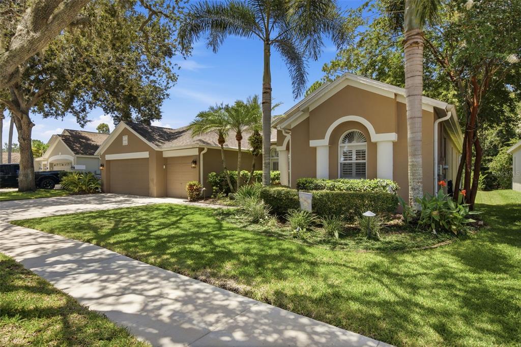 A tan single-story house with a two-car garage, palm trees, and a manicured front lawn — 10212 NEWINGTON PLACE, TAMPA, FL
